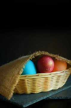 Coloful Easter eggs are in the Easter basket, burlap lies on top. Dark luxury Stock Photos