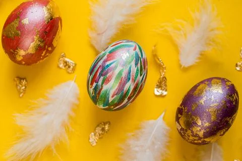 Cololrful painted Easter eggs on yellow background with foil and white feathers. Foto stock