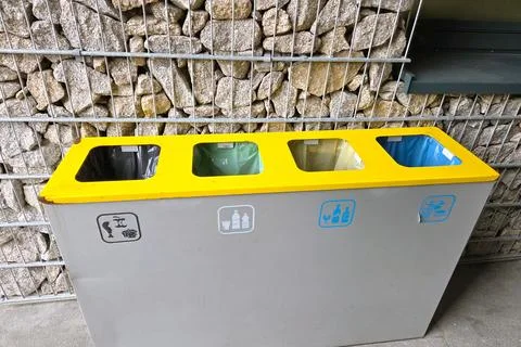 Color-coded recycling bins are set against a backdrop of stacked stones. desi Photos