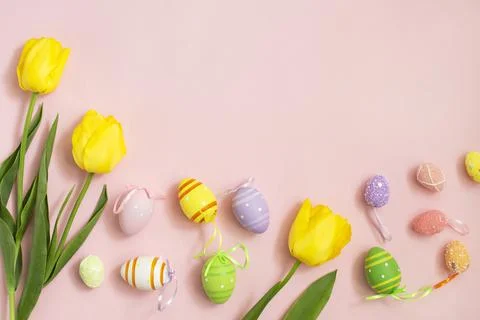 Color easter eggs and White yellow tulips on a pink background. Stock Photos