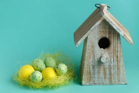 Color Easter eggs in nest on turquoise background with wooden vintage birdhouse Foto stock