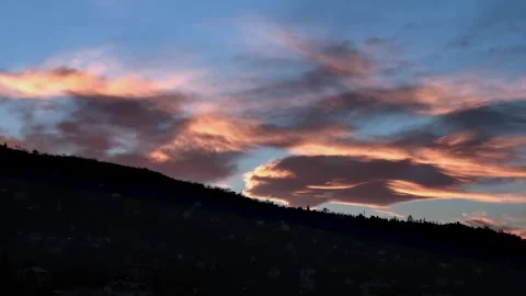 Color shifting sunset clouds above dark mountain ridge, evening sky transition Stock Footage 339438349