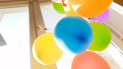 Colored balloons hang at the window. Slow motion. Green, blue, orange, red Stock Footage 91578472