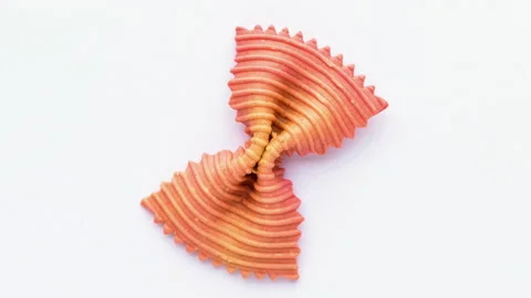 Colored bow tie pasta. Closeup single orange farfalle on white background. Stock Footage 136263118