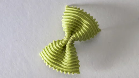 Colored bow tie pasta. Closeup single green farfalle on gray background. Stock Footage 136332688