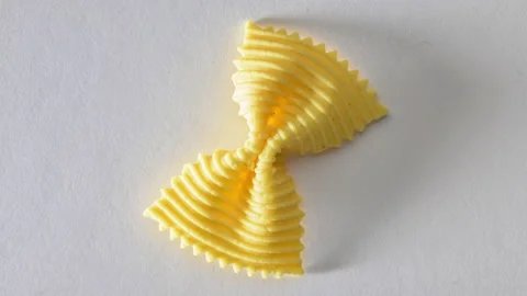 Colored bow tie pasta. Closeup single orange farfalle on gray background. Stock Footage 136491290