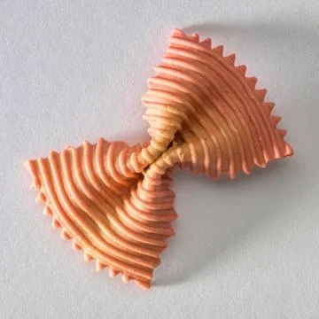 Colored bow tie pasta. Closeup single orange farfalle on gray background. Stock Photos