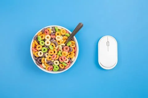 Colored breakfast cereal and computer mouse on a blue background, flat lay. Stock Photos
