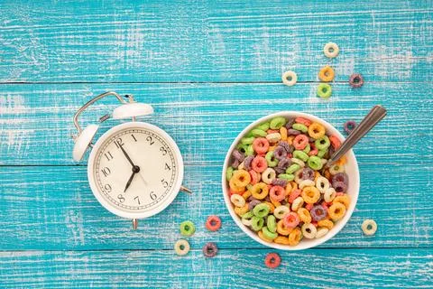 Colored breakfast cereals in a bowl and alarm clock on a blue wooden background. Foto stock