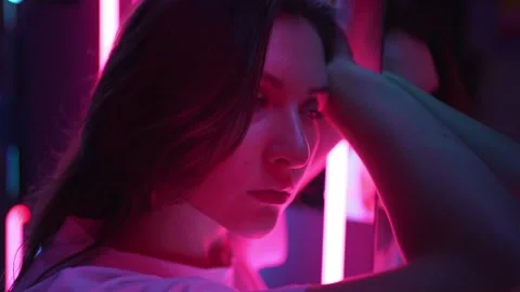 The colored bright pink lighting on the face of a beautiful young woman is close 動画素材 146208474