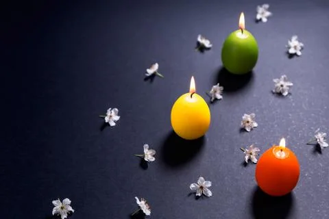 Colored candles in the shape of Easter egg with flowers on black background Stock Photos