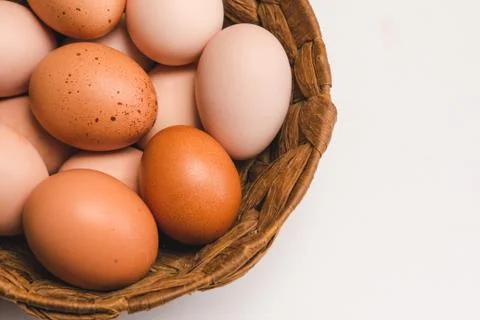 Colored chicken eggs in a wicker brown basket on a light background Stock Photos