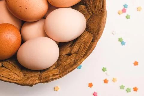 Colored chicken eggs in a wicker brown basket and pastry decorations Stock Photos
