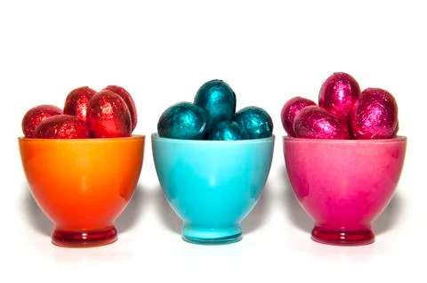 Colored chocolate easter eggs in glass cups of the same color Stock Photos