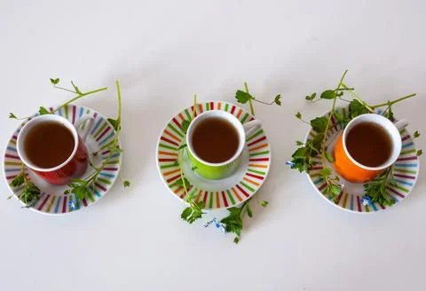 Colored cups of tea on a white table Stock Photos
