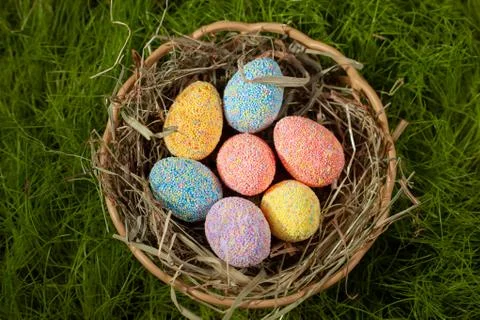 Colored decorative Easter eggs in a basket with hay on a green lawn Stock Photos