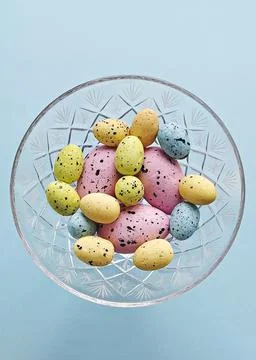 Colored decorative easter eggs in crystal vase on blue background, top view Stock Photos