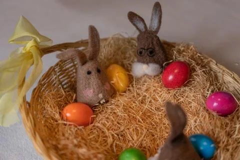 Colored easter eggs and brown felt bunnies in nest of straw in straw basket. Stock Photos