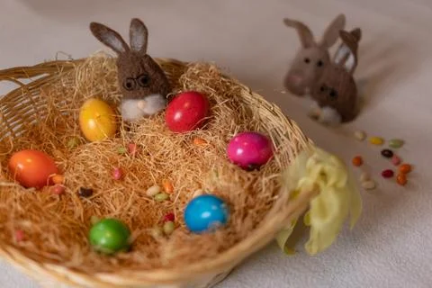 Colored easter eggs and one brown felt bunny in and two other outside the nest. 스톡 사진