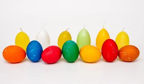 Colored easter eggs arranged in a row against a background of candles Stock Photos