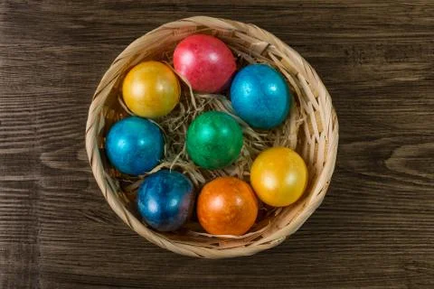 Colored Easter eggs in a basket on rustic wooden table. Stock Photos