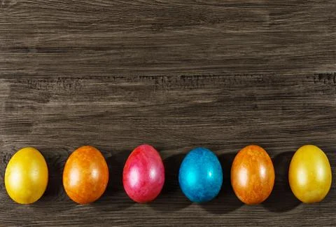 Colored Easter eggs in a basket on rustic wooden table. Stock Photos