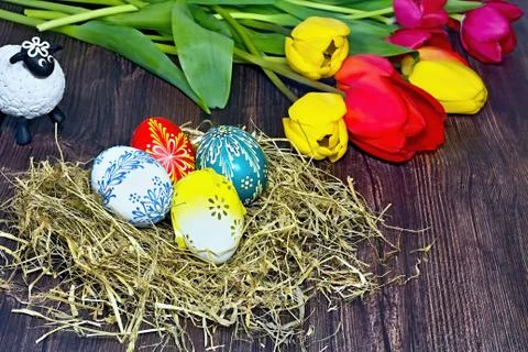 Colored Easter eggs deposited in the hay on a wooden board with a tulip backg Stock-Fotos