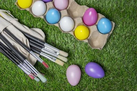 Colored Easter eggs in egg carton on grass with paint brushes Stock Photos