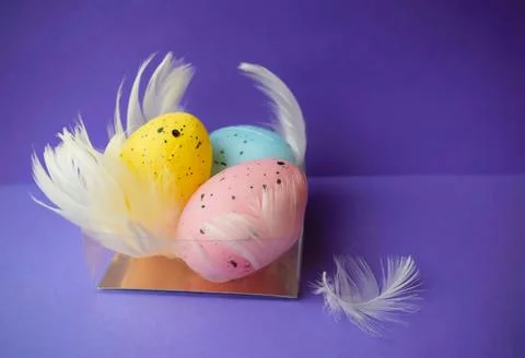 Colored Easter eggs with feathers in a transparent stand on a purple background Stock-Fotos