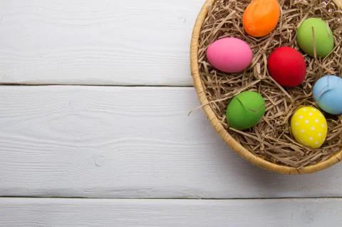 Colored easter eggs on nest beasket on white wooden background top white Stock Photos