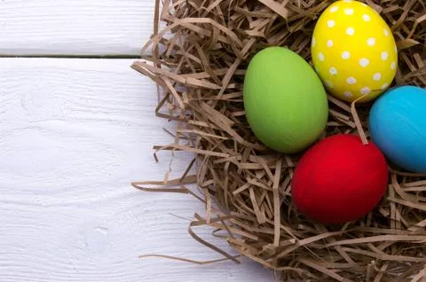 Colored easter eggs in nest top view on white wooden background Stock Photos
