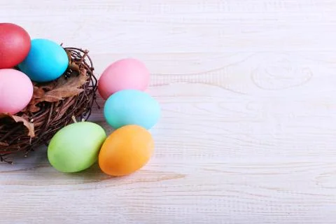 Colored Easter eggs in a nest, on a white wooden table. Stock Photos