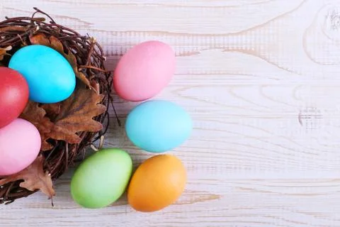 Colored Easter eggs in a nest, on a white wooden table. Stock Photos