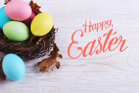 Colored Easter eggs in a nest, on a white wooden table. Text, happy easter. Stock Photos