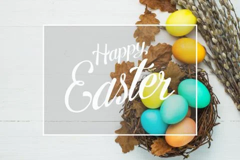 Colored Easter eggs in the nest on a white table, top view Stock Photos