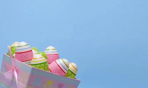 Colored Easter eggs in paper basket pastel colors on blue background. Stock Photos