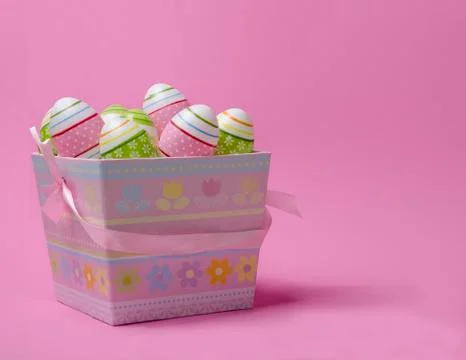 Colored Easter eggs in paper basket pastel colors on pink background. Easter Stock Photos