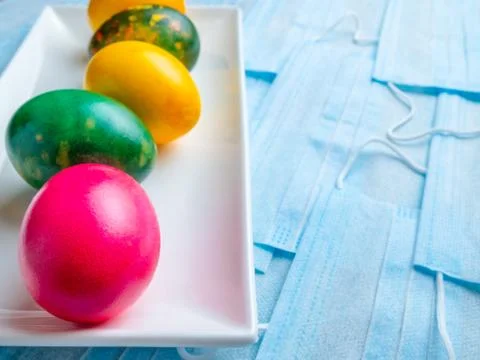 Colored Easter eggs on a white plate on a background of blue medical masks. Stock Photos