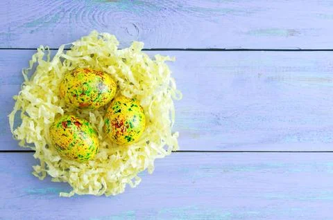Colored easter eggs in yellow paper shavings. On blue wooden background. Stock Photos