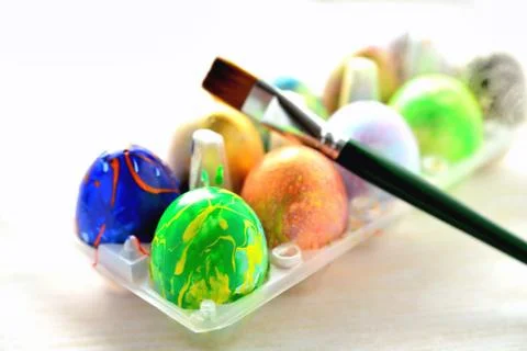 Colored eggs in a transparent box and an art brush, a blurred background, a b Stock Photos