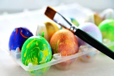 Colored eggs in a transparent box and an art brush, a blurred background, a b Stock Photos