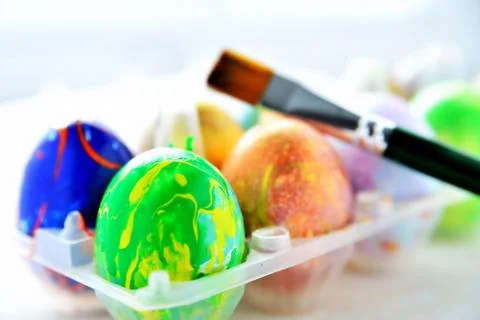 Colored eggs in a transparent box and an art brush, a blurred background, a b Stock Photos