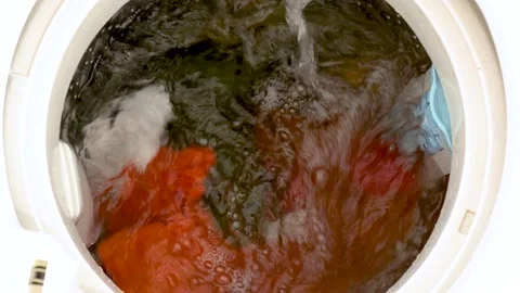 Colored laundry rotates inside the drum of a vertical washing machine Stock-Footage 239406254