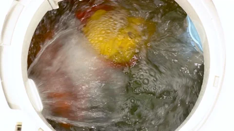 Colored laundry rotates inside the drum of a vertical washing machine Video stock 239406259