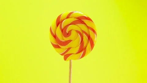 Colored lollipop is spinning on a yellow background. Candy on a stick Stock Footage 164803597
