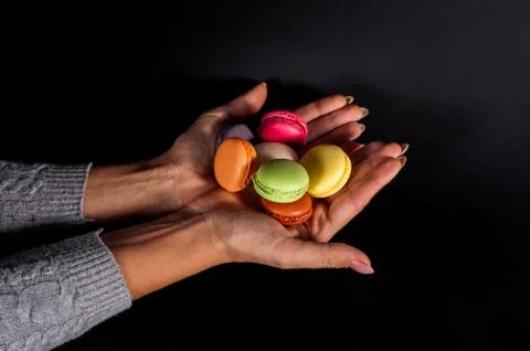 Colored macaroons in palms on a black background. Stock Photos