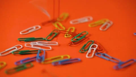 Colored paper clips fall on the orange table. school supplies Stock Footage 140198283