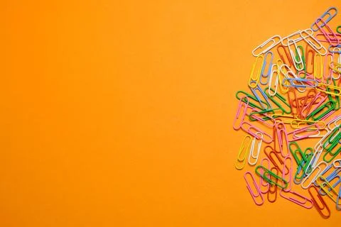 Colored paper clips on a orange background. Stock Photos