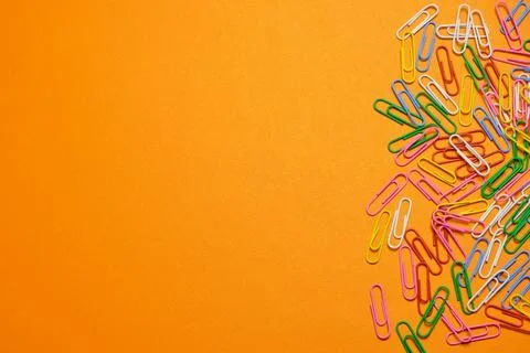 Colored paper clips on a orange background. Stock Photos