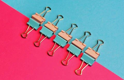 Colored paper clips on two backgrounds in half-pink and blue. Stationery. Stock Photos